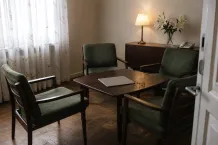 Stillsamt mötesrum med gröna fåtöljer runt ett lågt bord, vita liljor och tänd bordslampa.