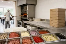 Pizzabagare skjuter in en pizza i ugnen bredvid degbollar och uppradade fyllningar.